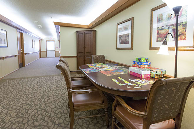 A cozy interior setting with a table and chairs, featuring board games and framed artwork on the walls.
