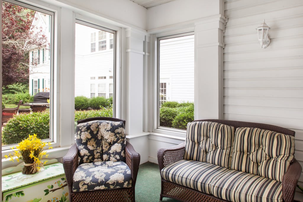 A bright sunroom with wicker chairs and patterned cushions, surrounded by large windows.