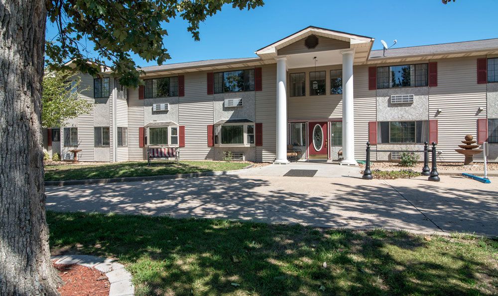 A two-story residential building with prominent columns, surrounded by trees and a well-maintained lawn.