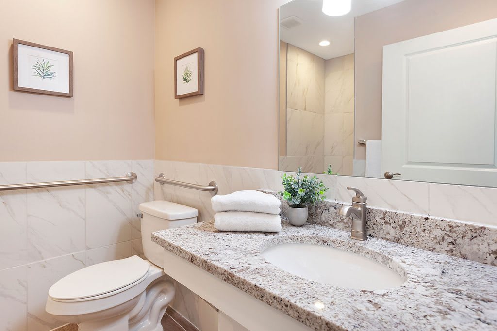 A modern bathroom with a granite countertop, neatly folded towels, and a potted plant.
