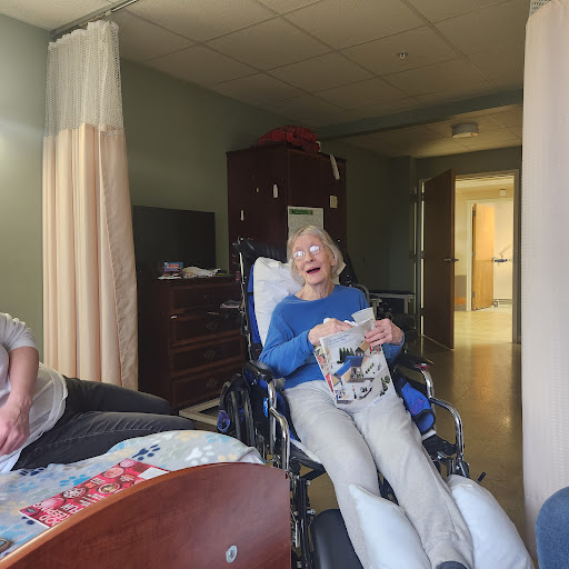 An elderly person in a wheelchair enjoying a moment with a caregiver in a hospital setting.