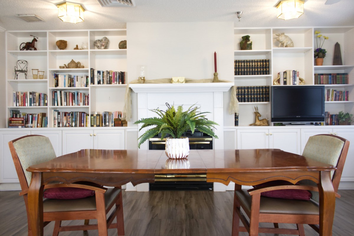 A cozy dining room featuring a wooden table and chairs, surrounded by bookshelves filled with books and decorative items.
