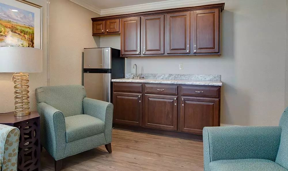 A cozy kitchenette with brown cabinets and two armchairs.
