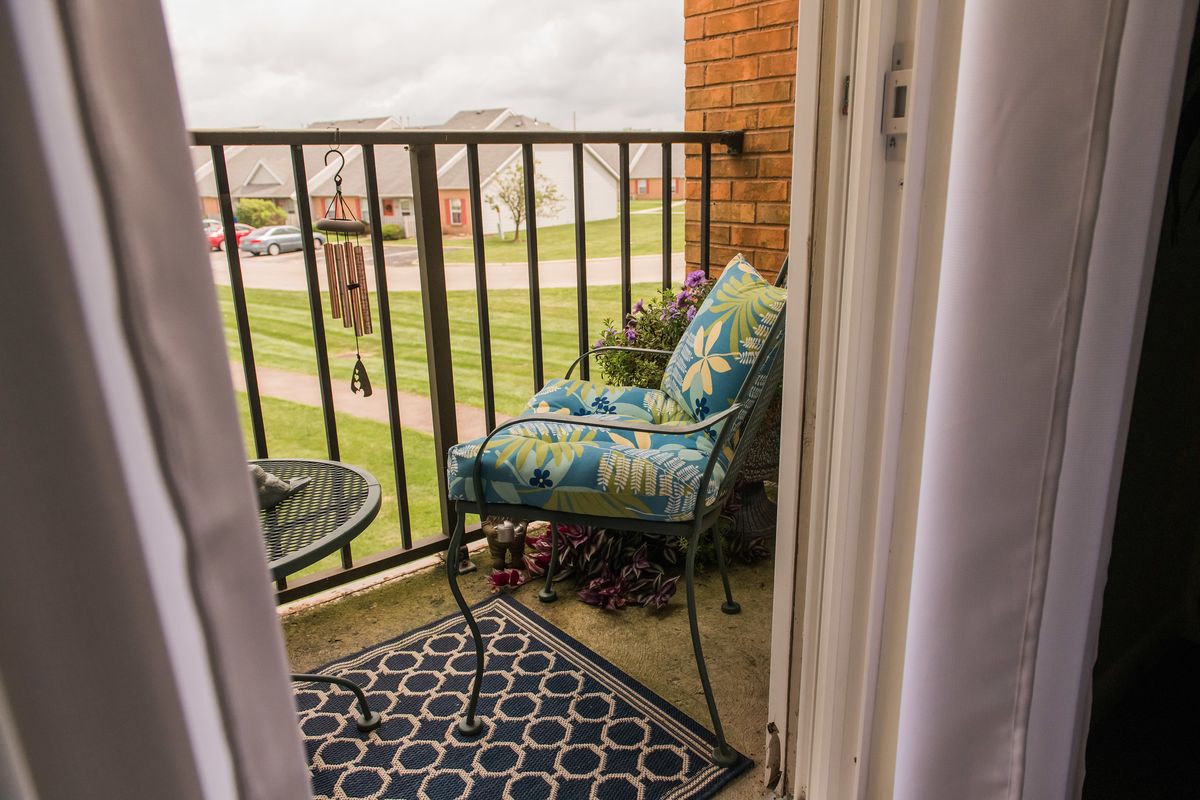 A cozy balcony with a cushioned chair and small table overlooking a grassy area.