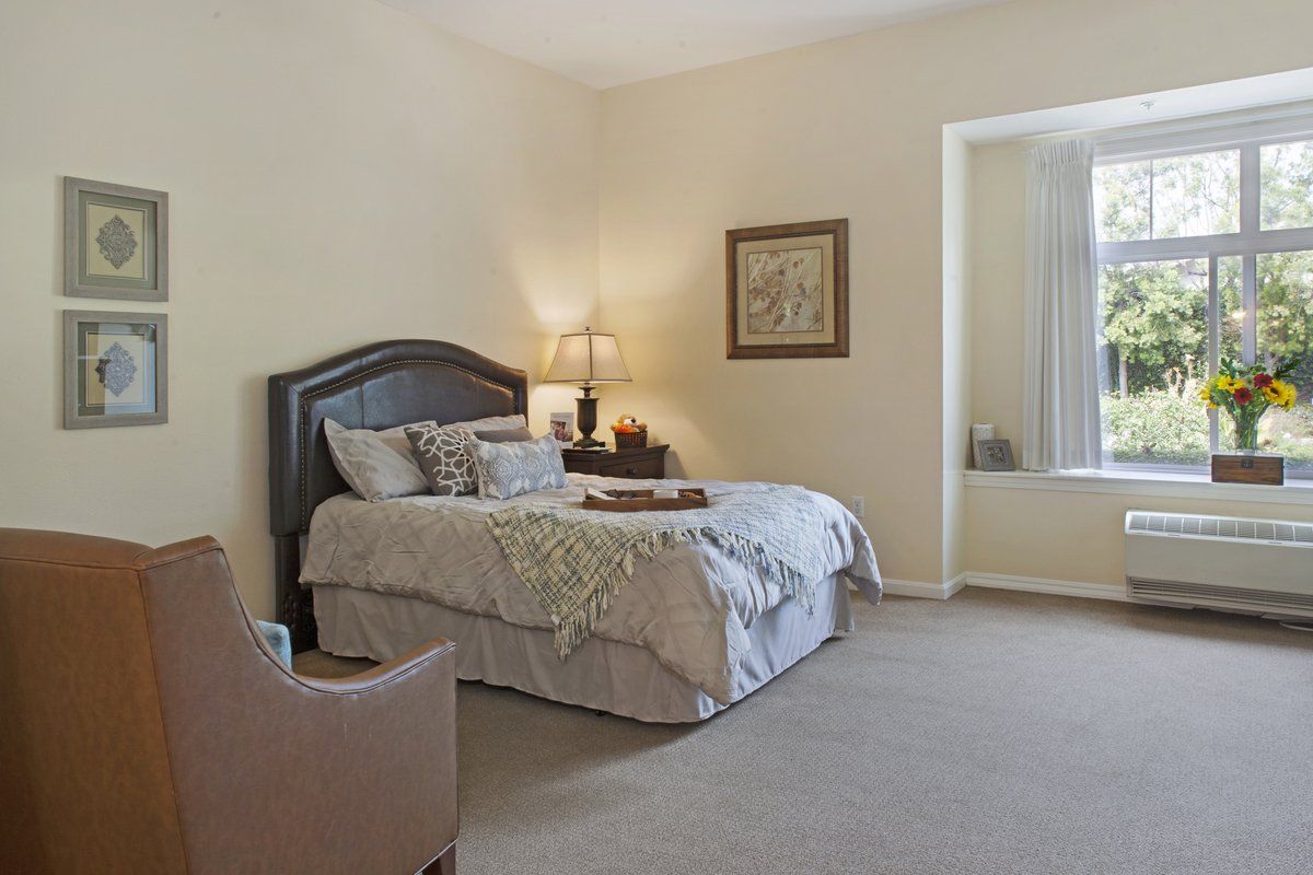 A cozy bedroom with a neatly made bed, nightstand, and comfortable chair.
