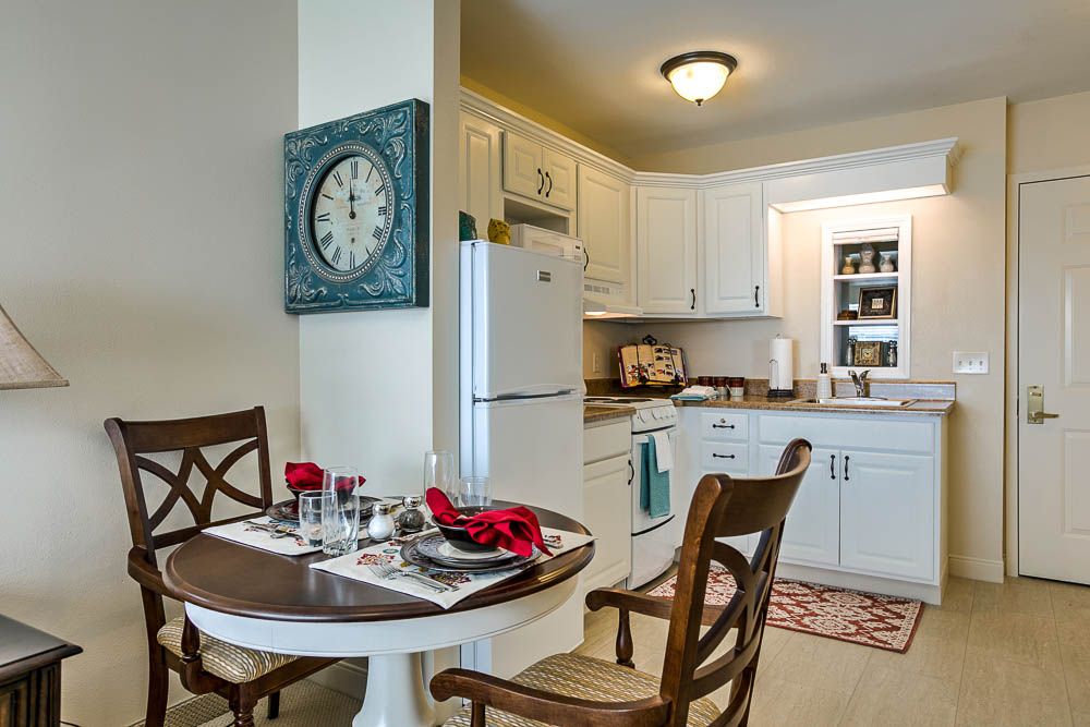A cozy kitchen and dining area featuring a small table set for two, surrounded by classic white cabinetry and modern appliances.