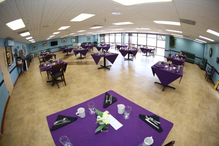 A banquet hall with tables set up with purple tablecloths, ready for an event.