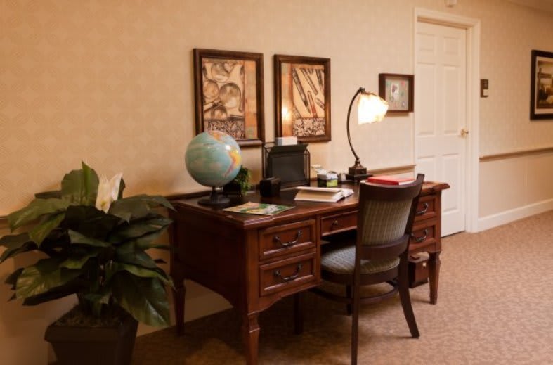A cozy office setup featuring a wooden desk with a globe, lamp, and books in a warmly lit room.