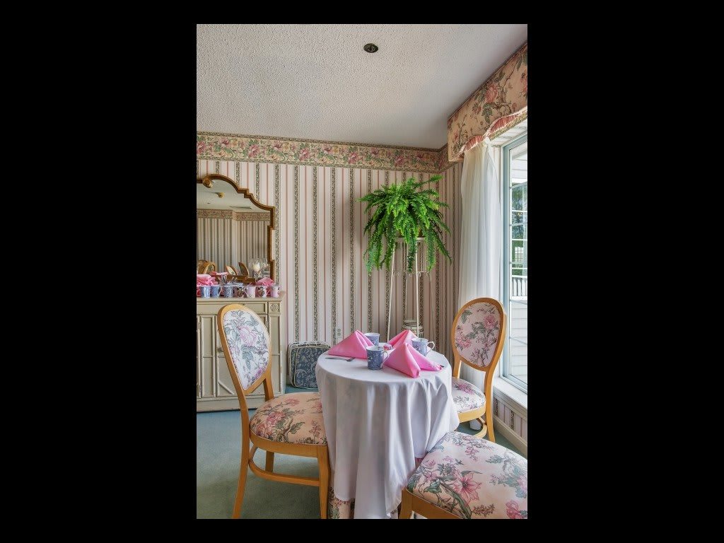 A charming dining nook with floral upholstered chairs and a table set with pink napkins, complemented by decorative wallpaper and natural light.