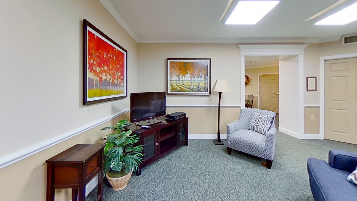A cozy living room featuring a television, armchair, and vibrant artwork on the walls.