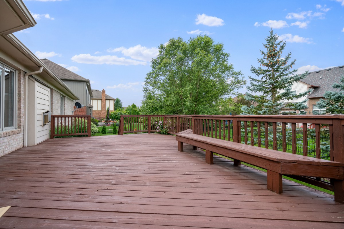 A spacious wooden deck with built-in benches, surrounded by greenery and neighboring houses.