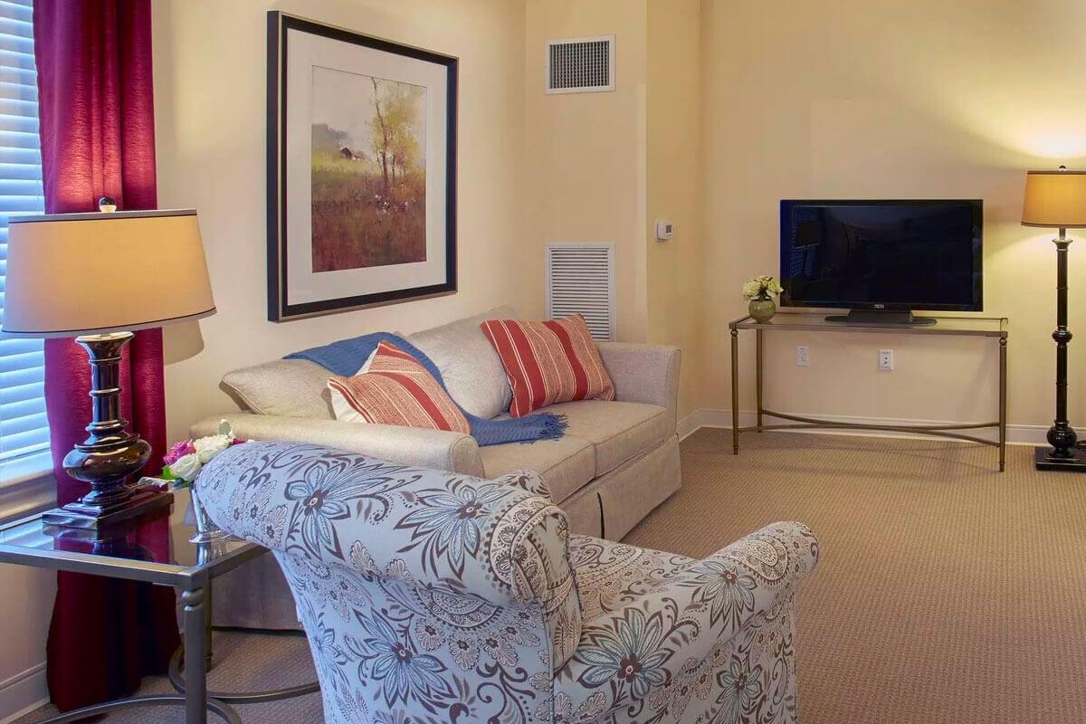 A cozy living room with a sofa, patterned armchair, and television.