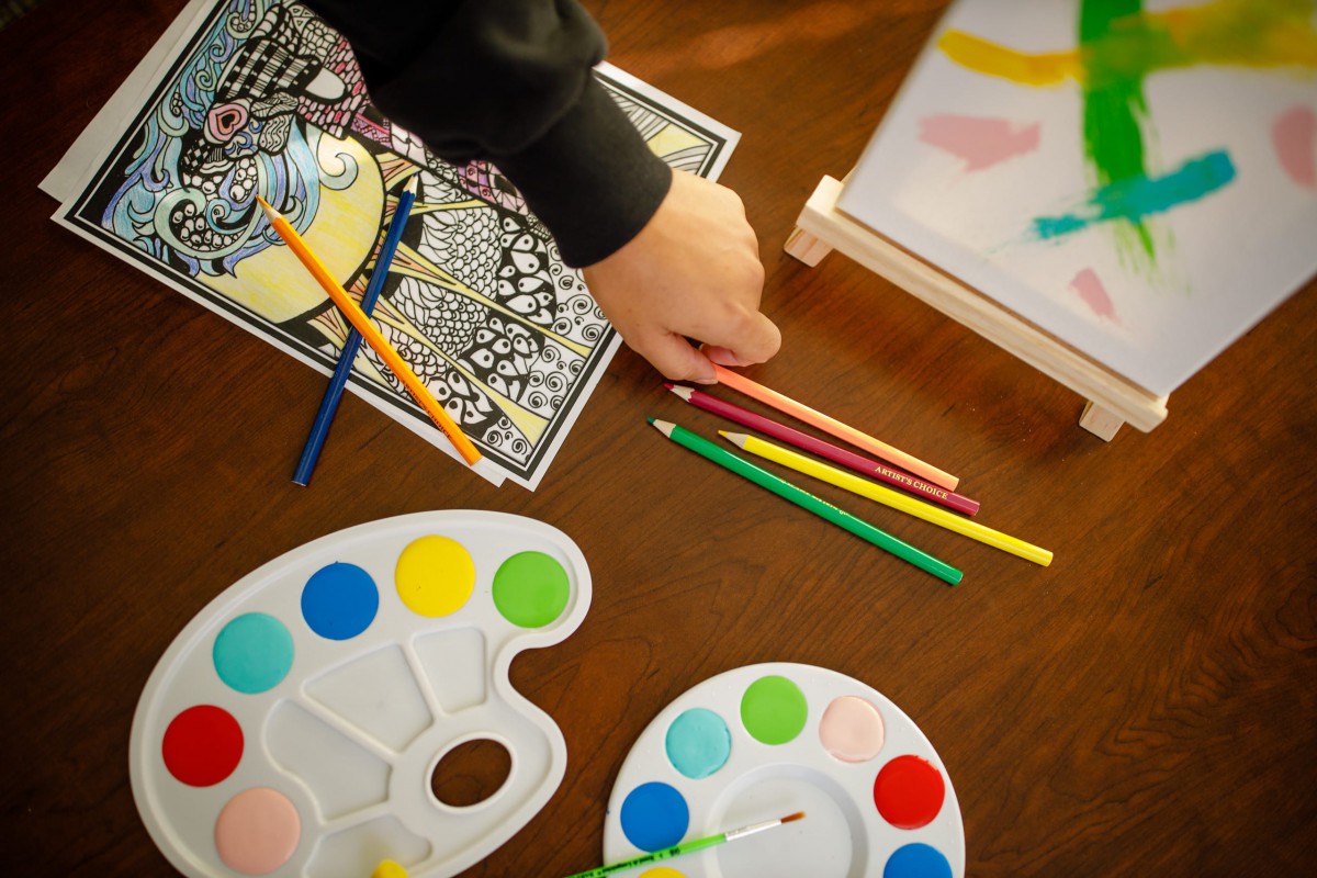 A creative setup with colored pencils, paint palettes, and coloring sheets on a table.