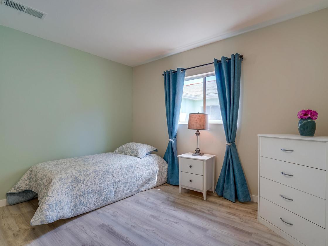 A minimalist bedroom with a single bed, blue curtains, and a lamp on the nightstand.