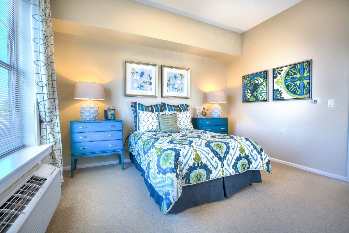 A modern bedroom with vibrant decor, featuring a colorful bedspread and matching art pieces on the walls.