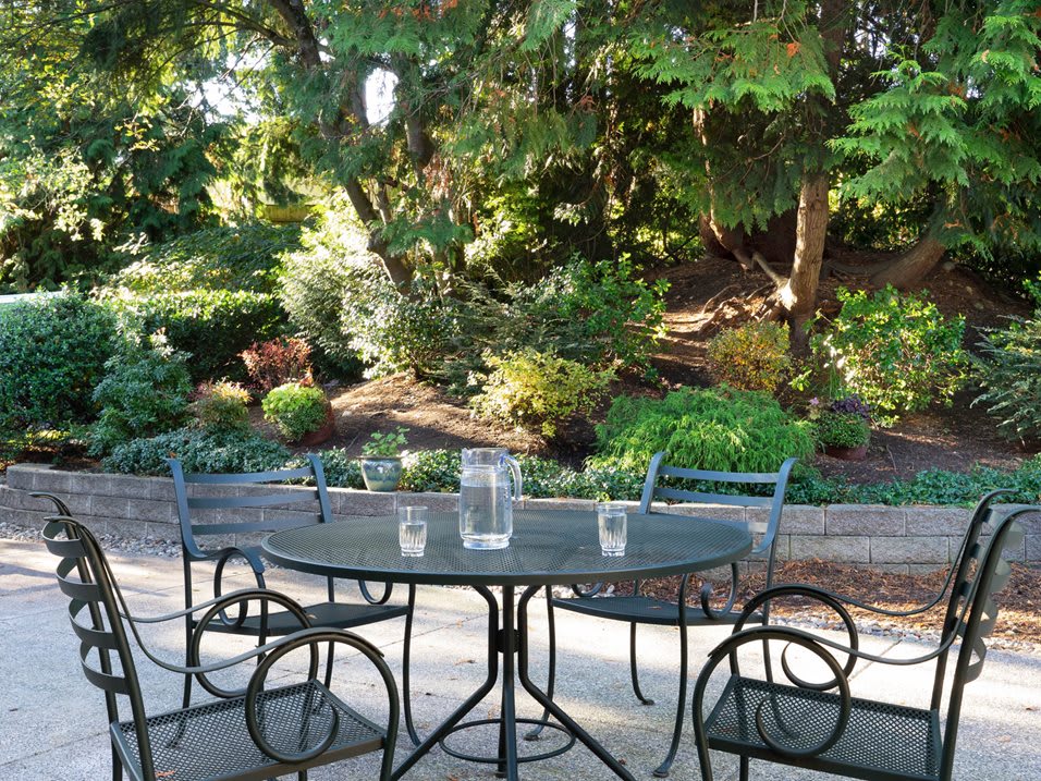 A serene patio setting with a metal table and chairs surrounded by lush greenery.