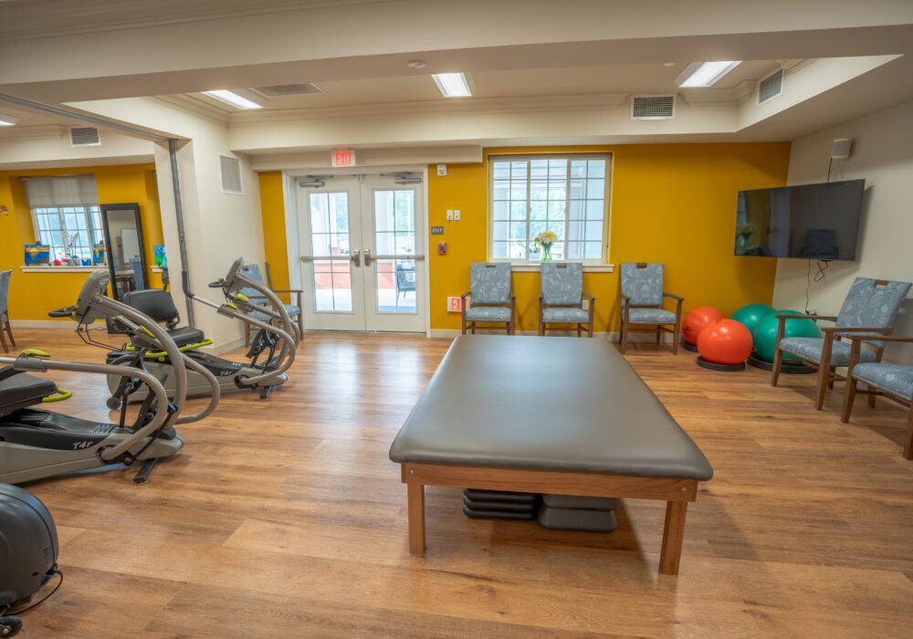 A well-equipped fitness and therapy room with exercise machines and a padded table.