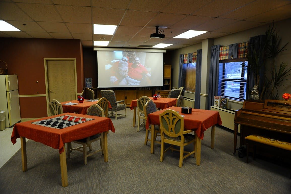 A room with several tables covered in red tablecloths, equipped with a large projector screen playing a video.
