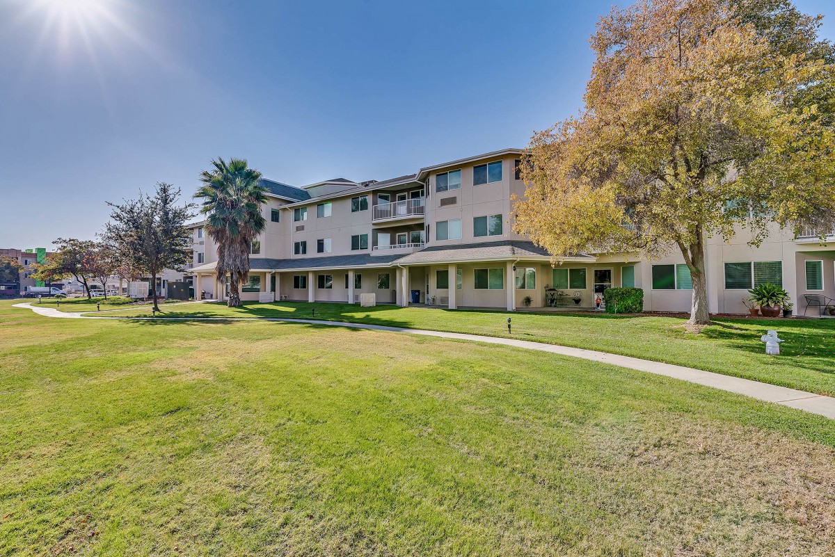 A residential apartment building with a well-maintained lawn and trees surrounding it.