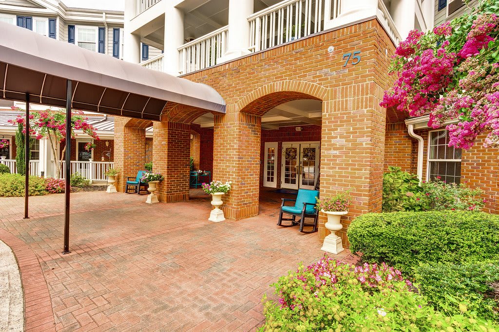 A welcoming brick building entrance with patio chairs and vibrant flowers.