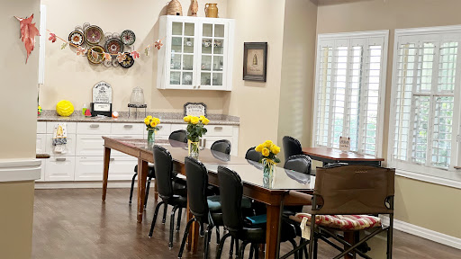 A cozy dining area featuring a long wooden table adorned with fresh flowers, surrounded by comfortable chairs and elegant cabinetry.