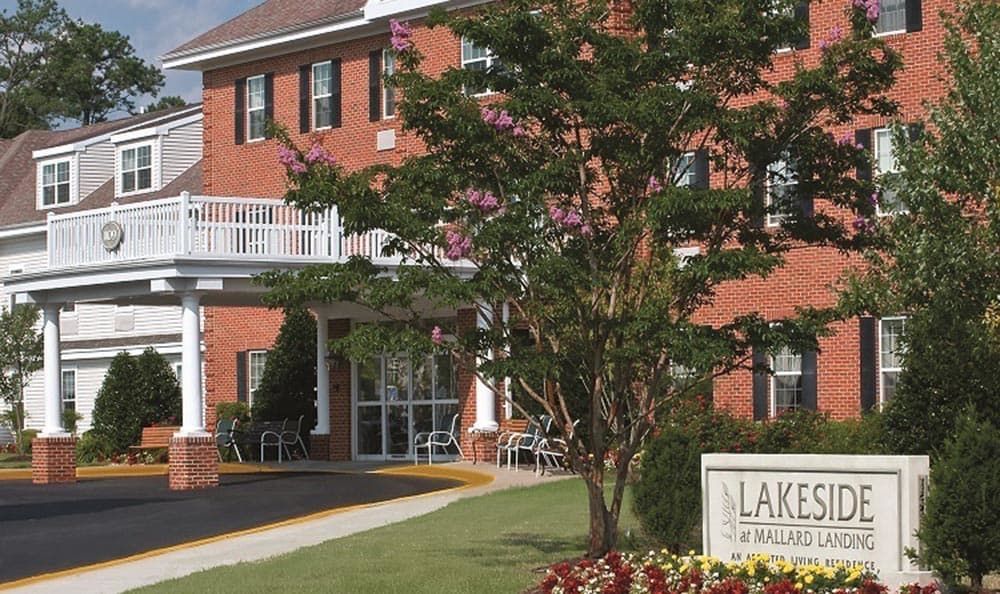 A brick building with a landscaped entrance and a sign in front.
