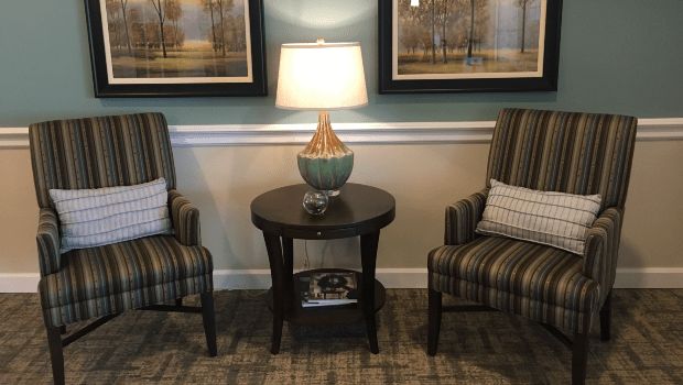 A cozy living room setup featuring two striped armchairs flanking a round wooden table with a stylish lamp and framed artwork above.