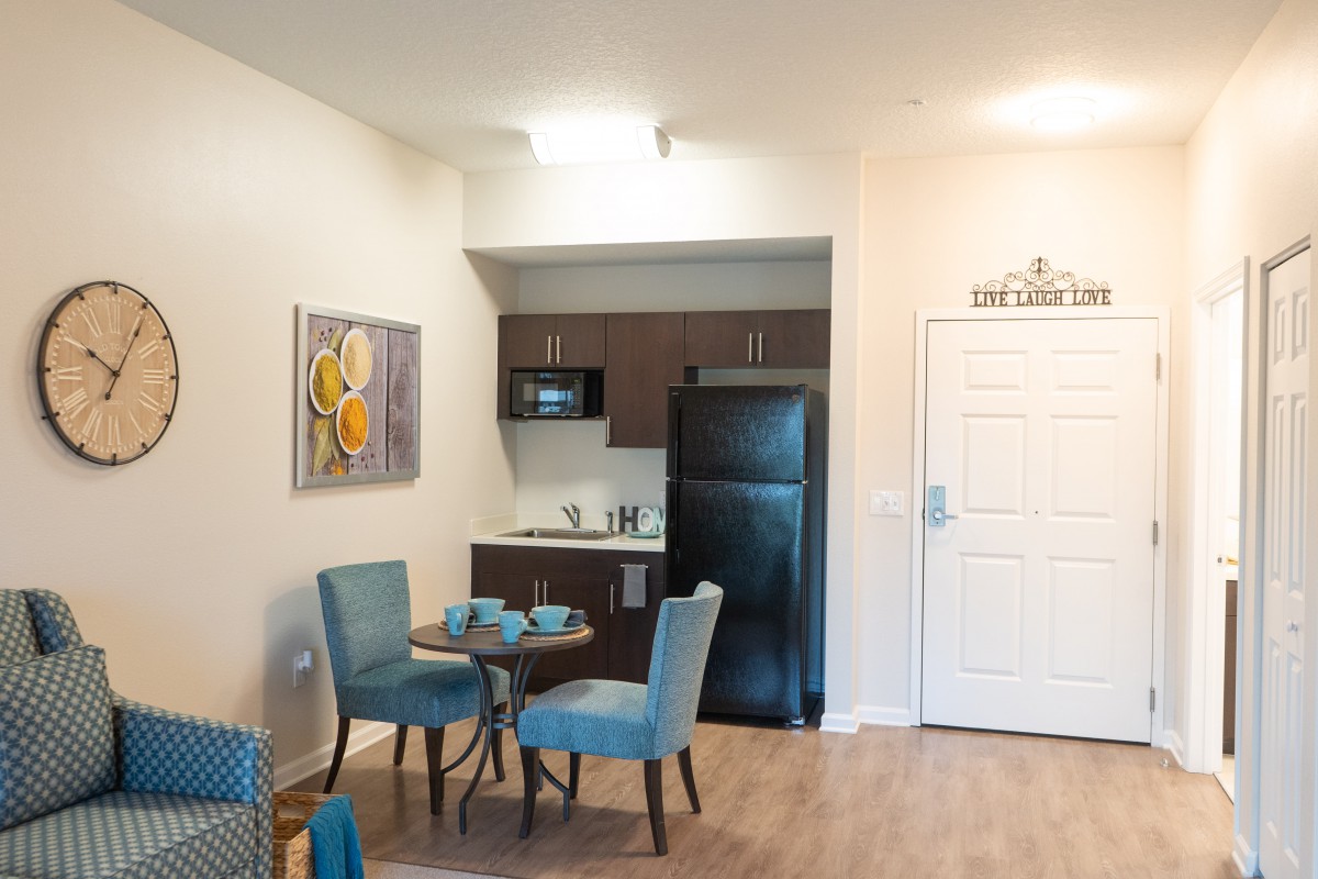A cozy apartment dining area with a small kitchenette and stylish blue chairs.
