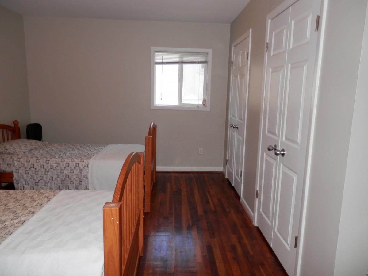 A simple bedroom with two twin beds and wooden flooring.