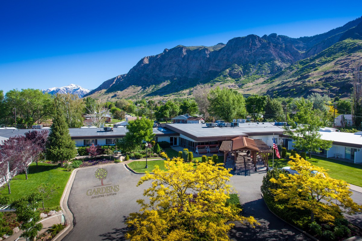 A scenic view of a building surrounded by lush greenery and majestic mountains under a clear blue sky.