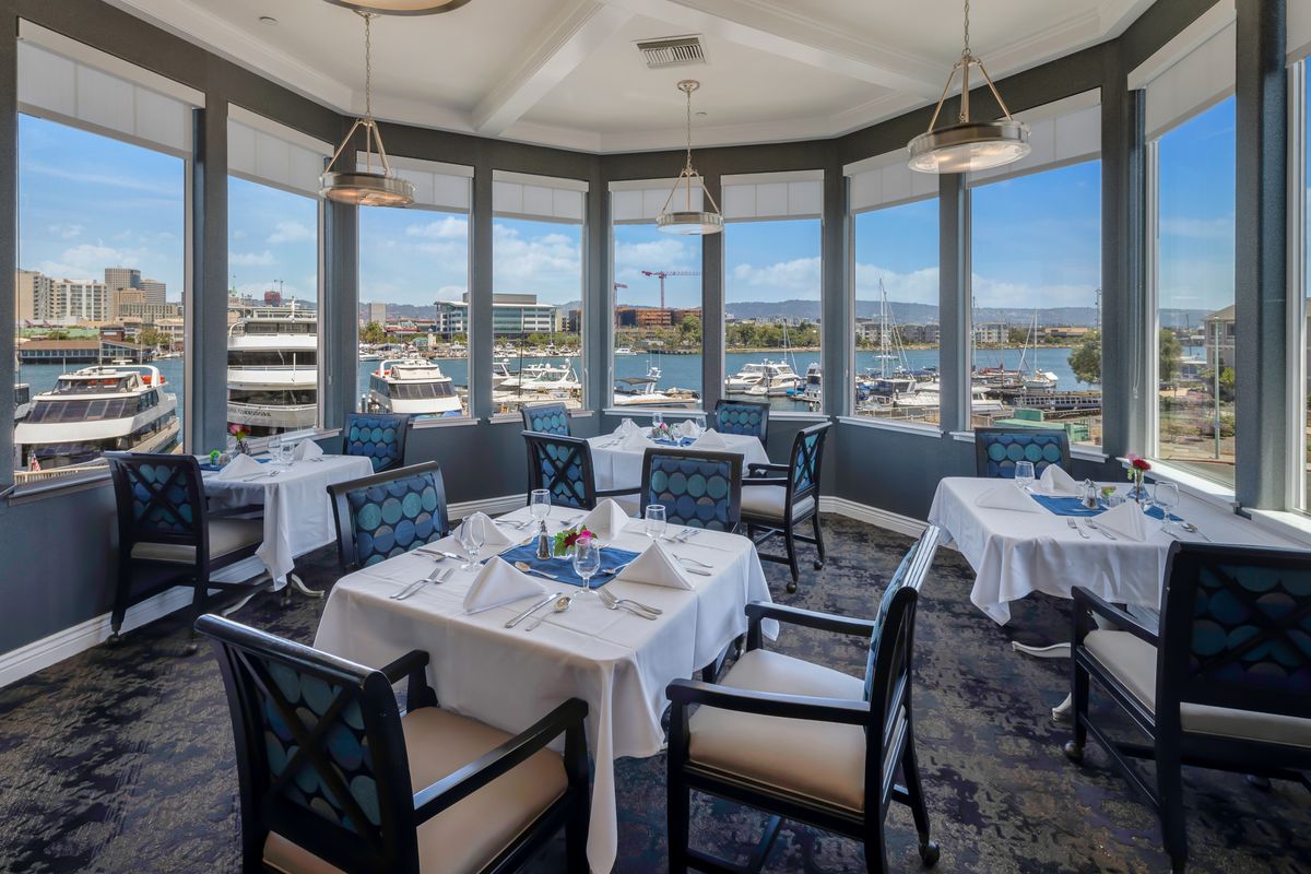 A waterfront restaurant with a scenic marina view, featuring elegantly set tables and comfortable seating.