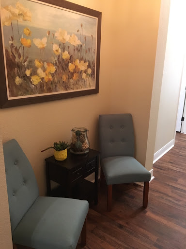 A cozy corner featuring two blue chairs and a decorative plant, complemented by a floral artwork on the wall.