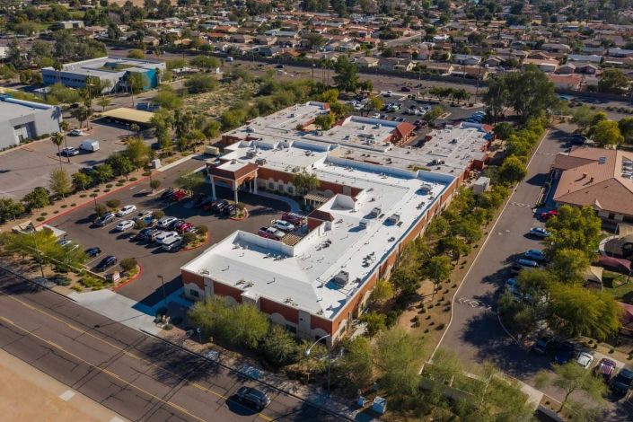 Aerial view of a large building surrounded by a parking lot and trees in an urban area.