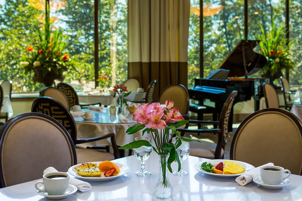 A beautifully set table with a breakfast menu and fresh flowers, overlooking a scenic view with a piano in the background.