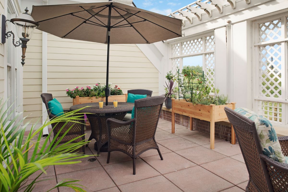 A cozy patio setup with a table, chairs, and an umbrella, surrounded by greenery and garden boxes.