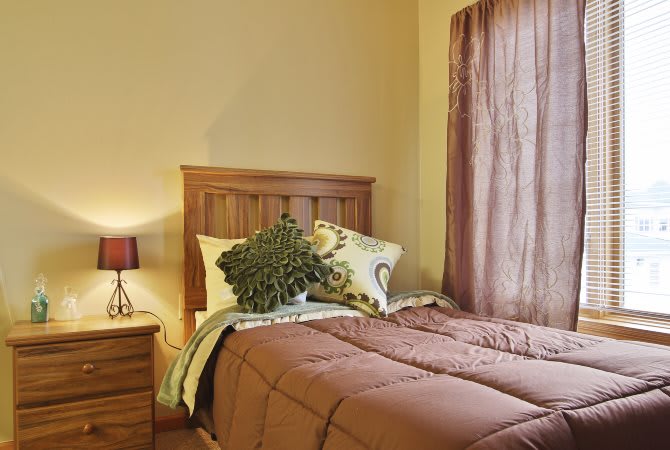 Cozy bedroom with a neatly made bed, nightstand, and lamp.