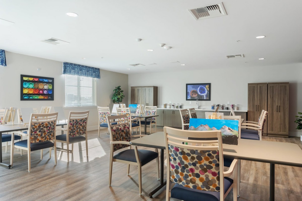 A modern dining room with neatly arranged tables and chairs, large windows, and bright lighting.