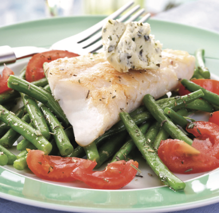 A delicious plate of fish served on a bed of green beans and cherry tomatoes, topped with herb butter.