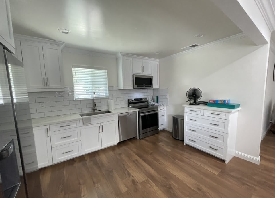 A modern kitchen with white cabinets and hardwood flooring.