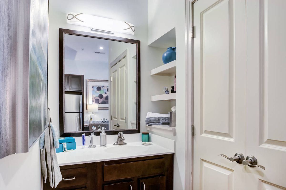A modern bathroom with a large mirror, sink, and neatly organized shelves.
