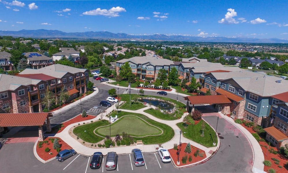 Aerial view of a residential complex with landscaped gardens and parking spaces, set against a backdrop of mountains and blue skies.