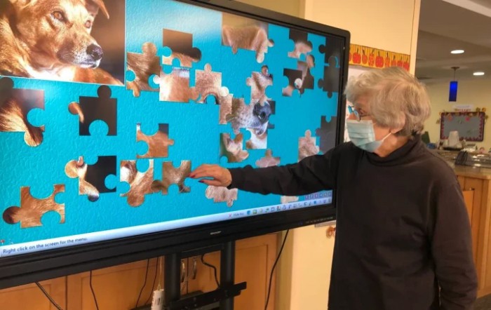 A senior individual interacts with a digital jigsaw puzzle on a large touchscreen.