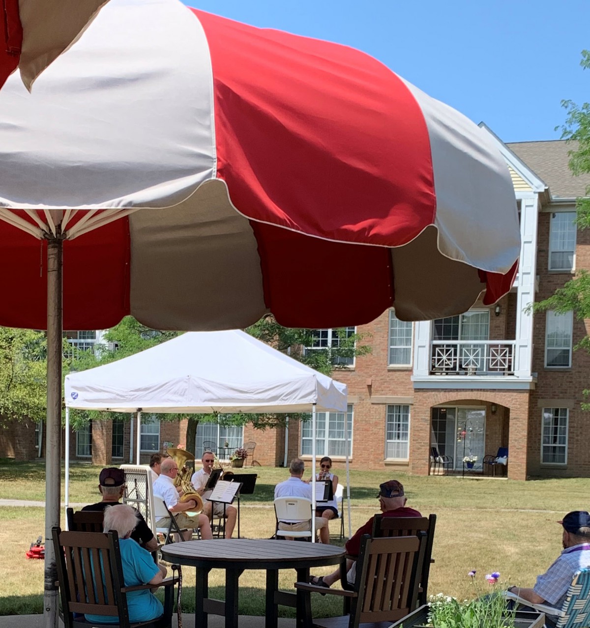 People relaxing under a large umbrella in an outdoor setting with a building in the background.