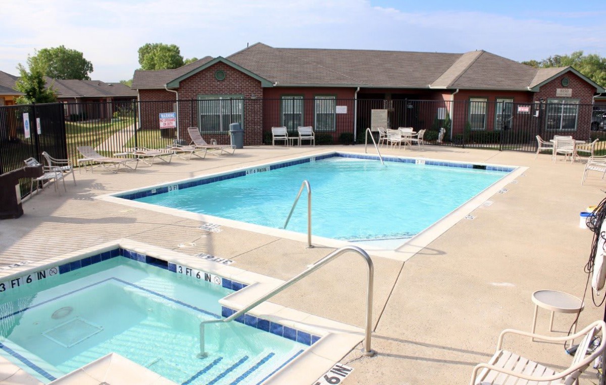 An outdoor pool area with a swimming pool, hot tub, and clubhouse seating.
