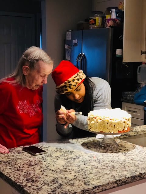 Two people decorating a cake together in the kitchen during a holiday gathering.