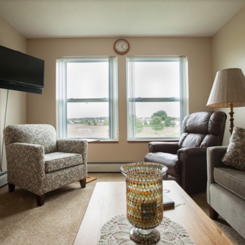 A cozy living room with armchairs, a sofa, and a coffee table in front of two large windows.