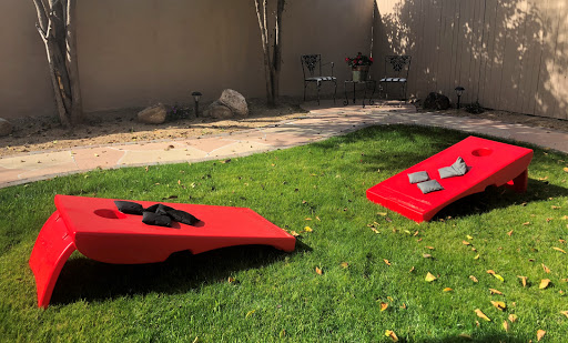 A sunny backyard setup featuring two red cornhole boards on a grassy lawn.