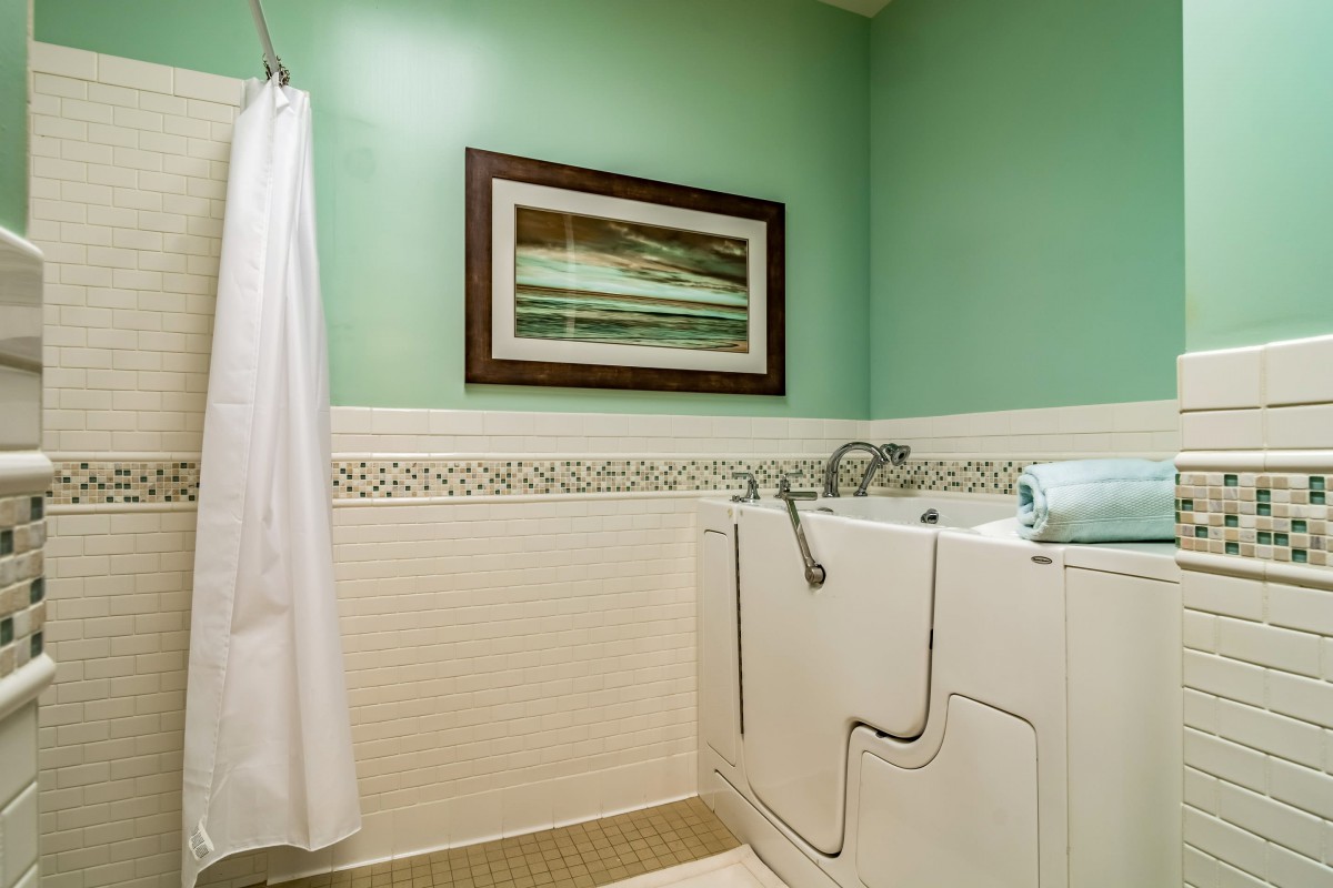 A bathroom with green walls, featuring a walk-in bathtub and shower curtain.