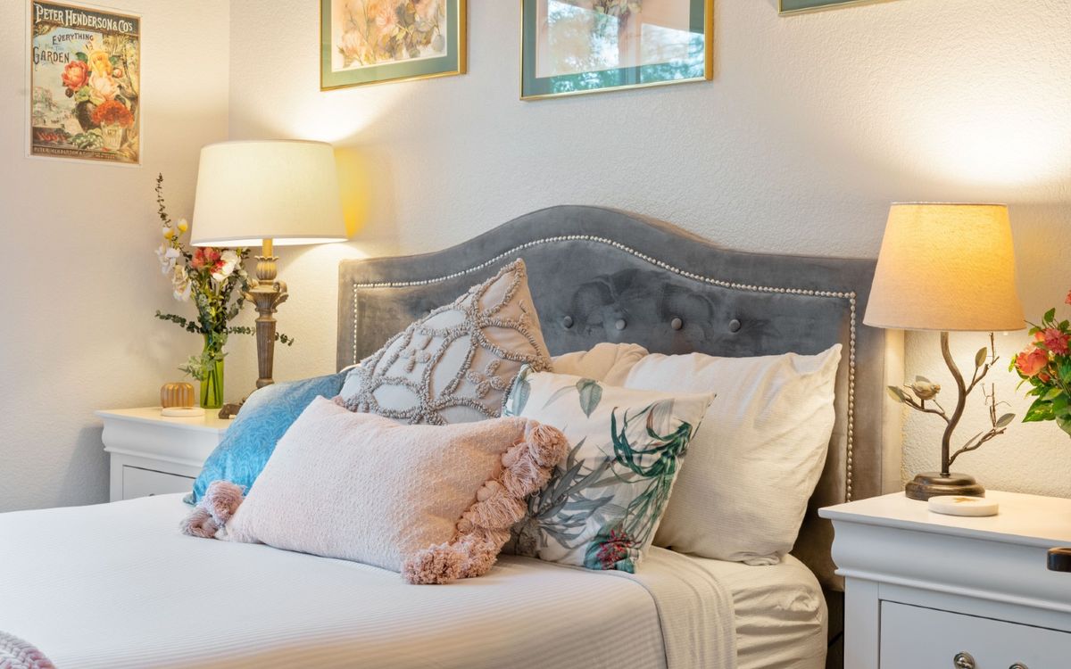 A cozy bedroom with a tufted headboard, a variety of decorative pillows, and soft lighting from a bedside lamp.