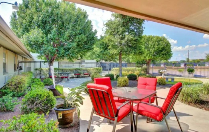 A cozy patio with red cushioned chairs overlooking a beautifully landscaped garden.